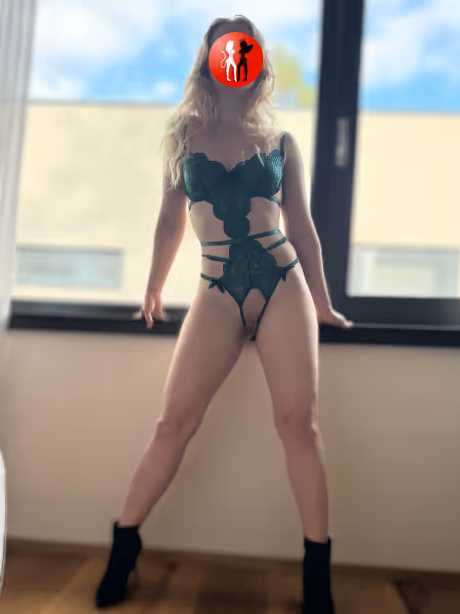 Escort Lady Luisa steht breitbeinig vor einem großen Fenster, gekleidet in ein grünes, verführerisch geschnittenes Dessous-Set mit verspielten Cut-outs. Ihre Pose ist selbstbewusst, dominant und zugleich voller erotischer Spannung. Die schwarzen Stiefeletten unterstreichen ihren sinnlichen Auftritt. Luisa Escort Lady in Magdeburg zeigt sich hier aufregend, sexy und bereit für prickelnde Abenteuer.